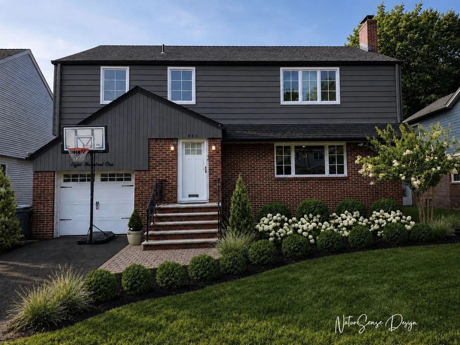 Front yard with a brick paver walkway and steps leading to a white front door, a low boxwood hedge, white hydrangeas, and ornamental grasses in front of a gray-sided home